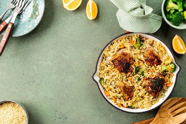 Sizzling high protein chicken orzo in a white skillet, garnished with fresh parsley and parmesan cheese.
