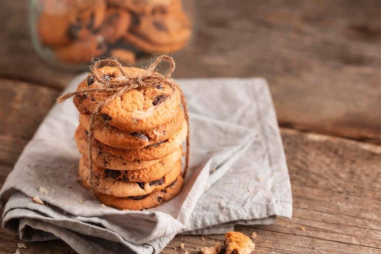 A stack of golden-brown high-protein chickpea breakfast cookies on a white plate, with one broken in half to show the soft, fluffy texture inside.