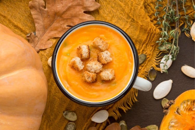 A rustic white bowl filled with creamy orange High-Protein Kabocha Squash Soup, garnished with toasted pumpkin seeds, coconut cream, and fresh thyme.