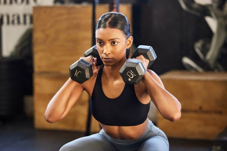 Woman performing a dumbbell shoulder press during a 35-minute full body HIIT workout at a gym.