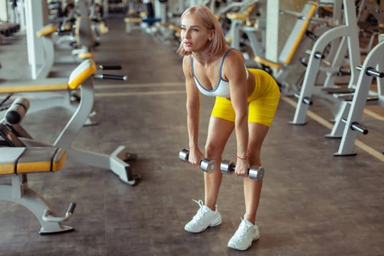 Woman performing Romanian deadlifts with dumbbells for a 20 minute low impact HIIT workout.