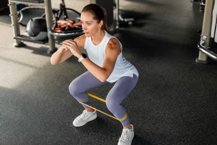 Woman Athlete performing a resistance band squat as part of a Resistance Band Progressive Overload plan.