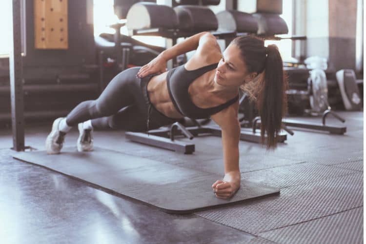 Woman performing a plank exercise during a 30-minute core superset workout in a gym.