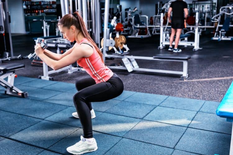 Woman performing a heavy dumbbell squat during a strength and core superset workout in the gym.