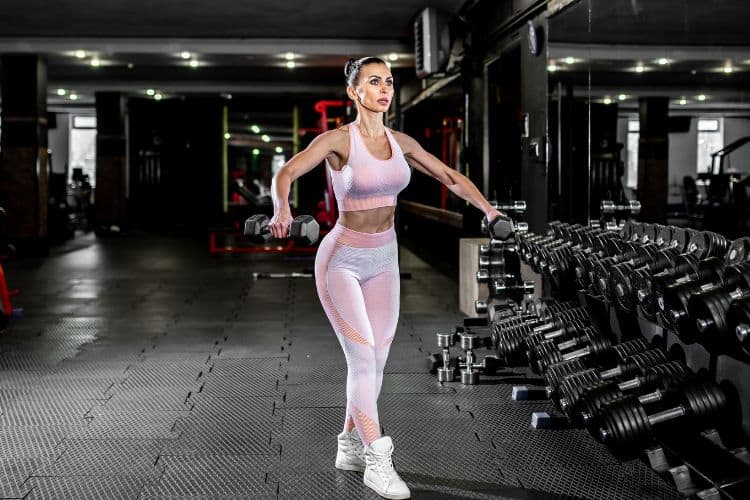 woman performing a dumbbell superset workout in a gym with a 5-day upper lower body split schedule.