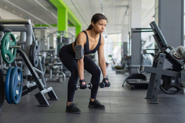Woman performing a low-impact dumbbell EMOM workout in a gym with a pair of light for dumbbells for Low-Impact Dumbbell EMOM Workout.