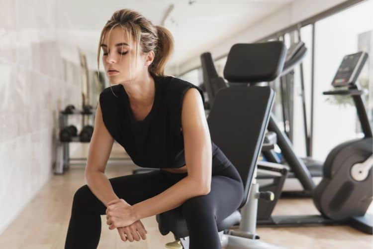 Female weightlifter resting on a bench in a gym, looking focused, representing a deload week for progressive overload.