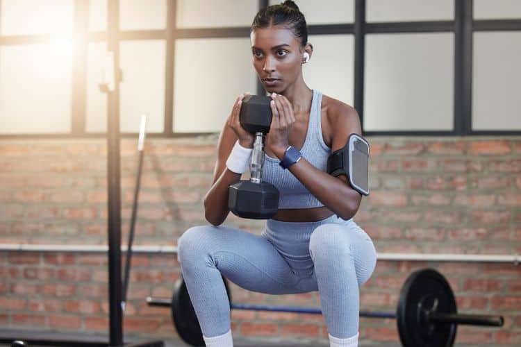 Woman doing a goblet squat with a dumbbell as part of a superset power workout program.